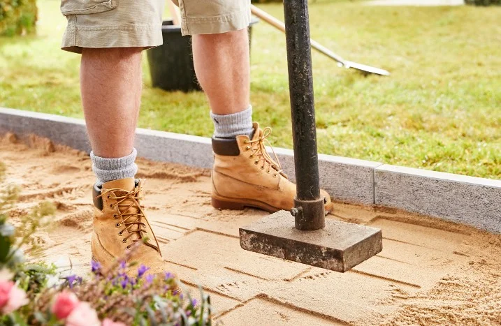 Person stampft Sand mit einem Werkzeug fest
